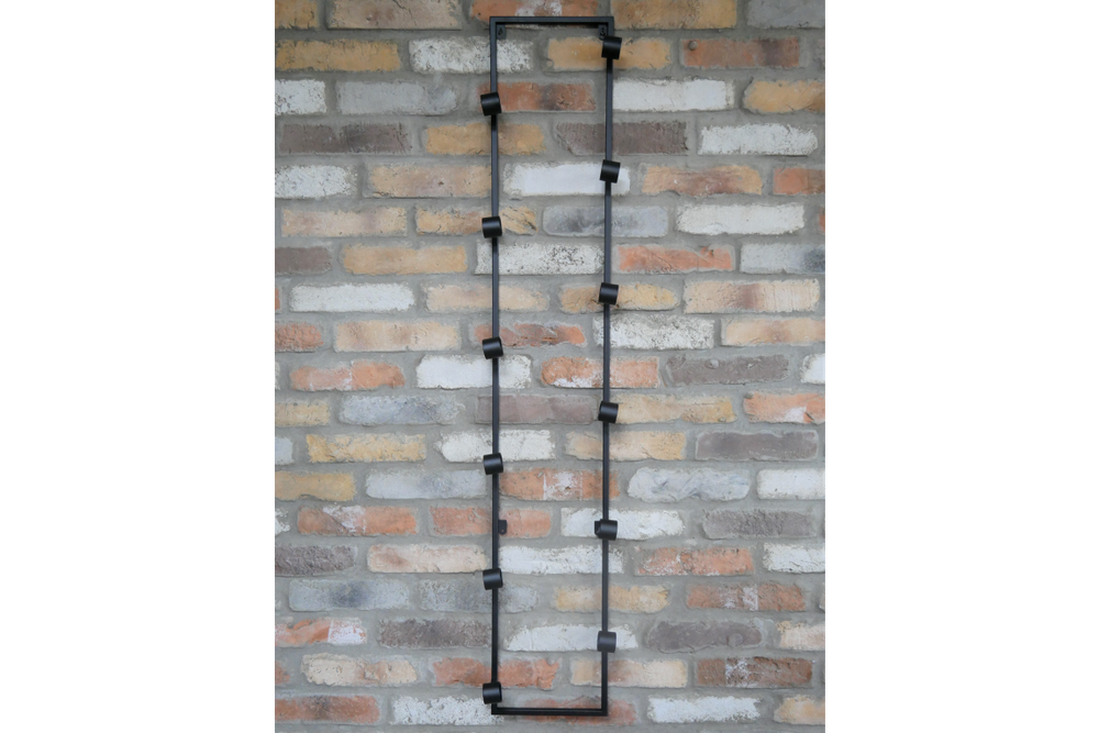 Tall black metal wine bottle holder with multiple circular holders mounted vertically on a brick wall.