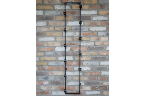 Tall black metal wine bottle holder with multiple circular holders mounted vertically on a brick wall.