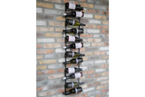 Vertical black metal wine bottle holder mounted on exposed brick wall, storing ten bottles horizontally.