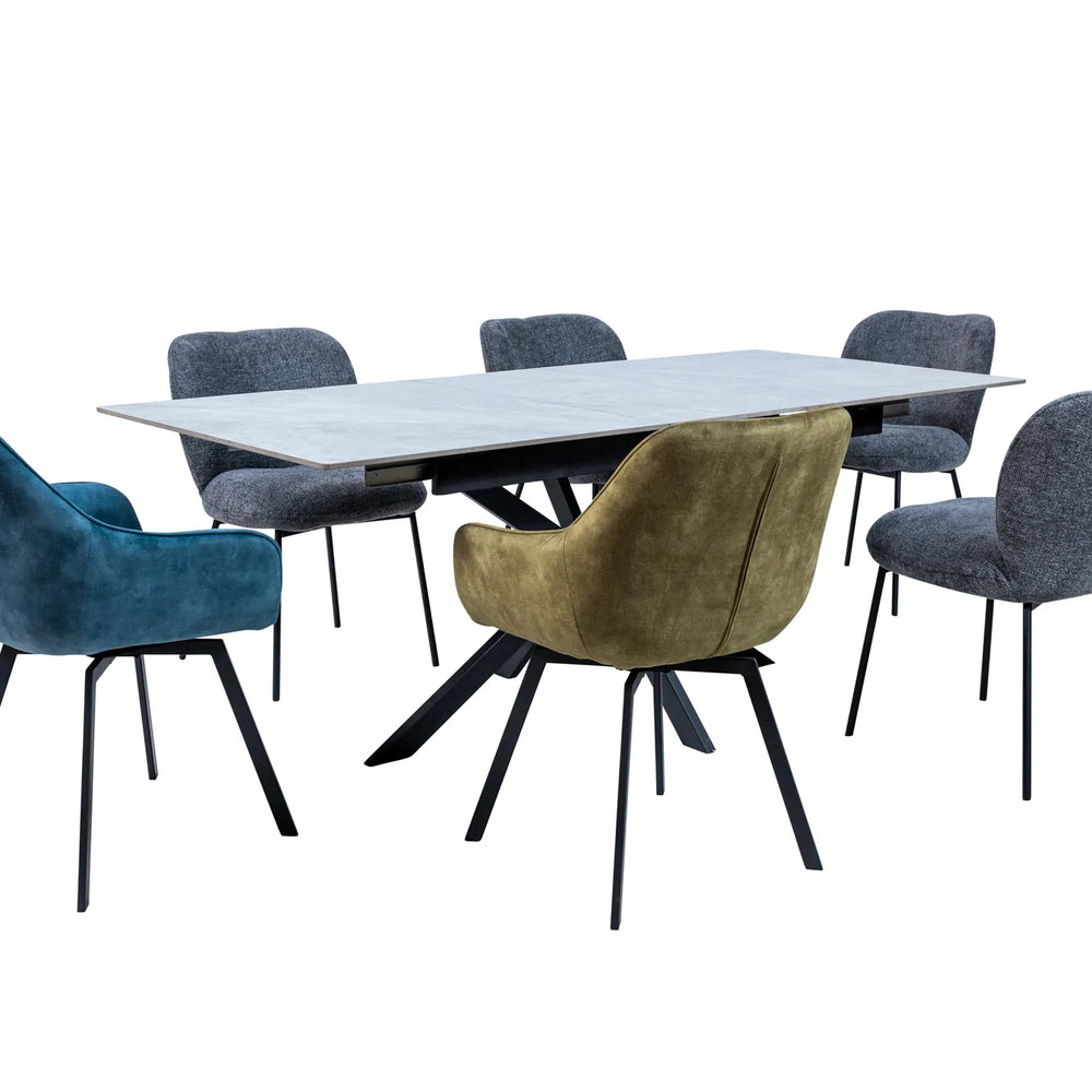 A modern dining set featuring a rectangular light gray stone-look table surrounded by five upholstered chairs in blue, olive green, and gray, with black metal legs, shown on a solid white background.