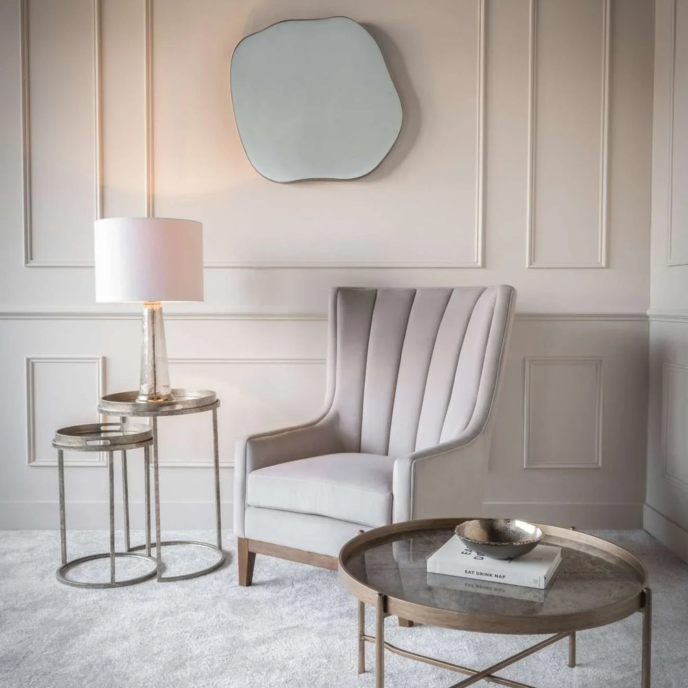 Elegant gold tray tables in a cozy living room with an armchair and wall mirror.