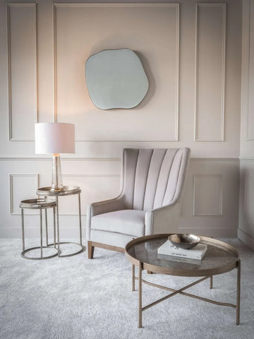 Elegant gold tray tables in a cozy living room with an armchair and wall mirror.