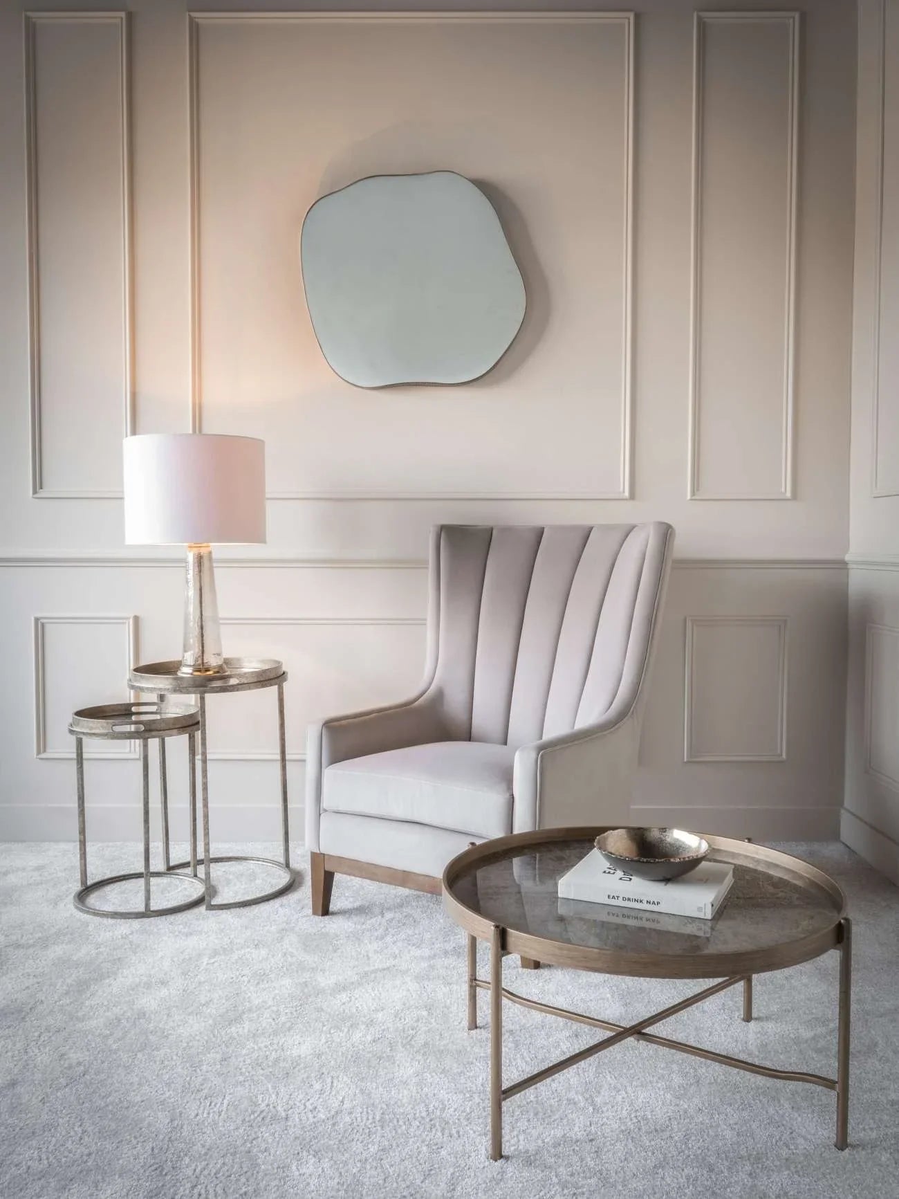 Elegant gold tray tables in a cozy living room with an armchair and wall mirror.