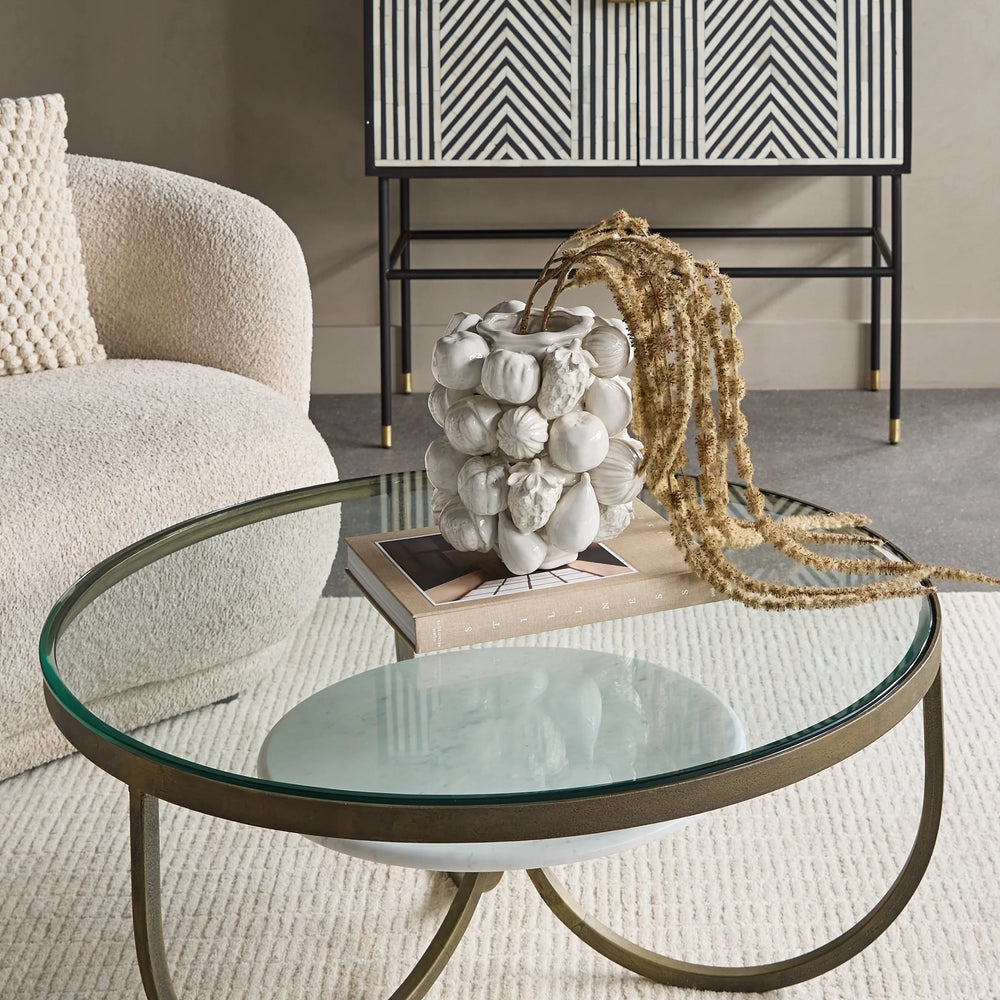 Round glass coffee table with gold iron legs in a stylish living room.