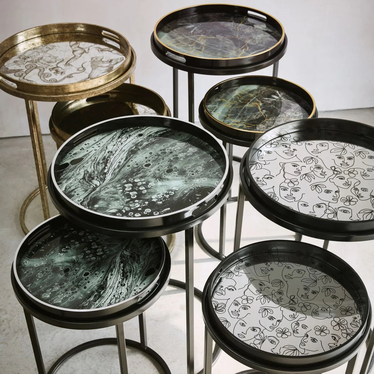 Assorted decorative tray tables with artistic patterns and sleek metal legs.