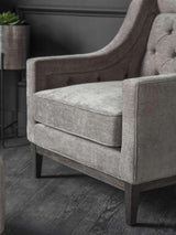 Warm grey armchair with buttoned backrest and dark wooden legs.