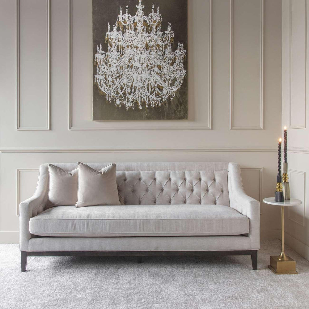 Ivory buttoned sofa in elegant room with chandelier artwork and side table.