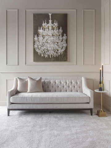 Ivory buttoned sofa in elegant room with chandelier artwork and side table.