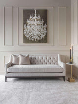 Ivory buttoned sofa in elegant room with chandelier artwork and side table.