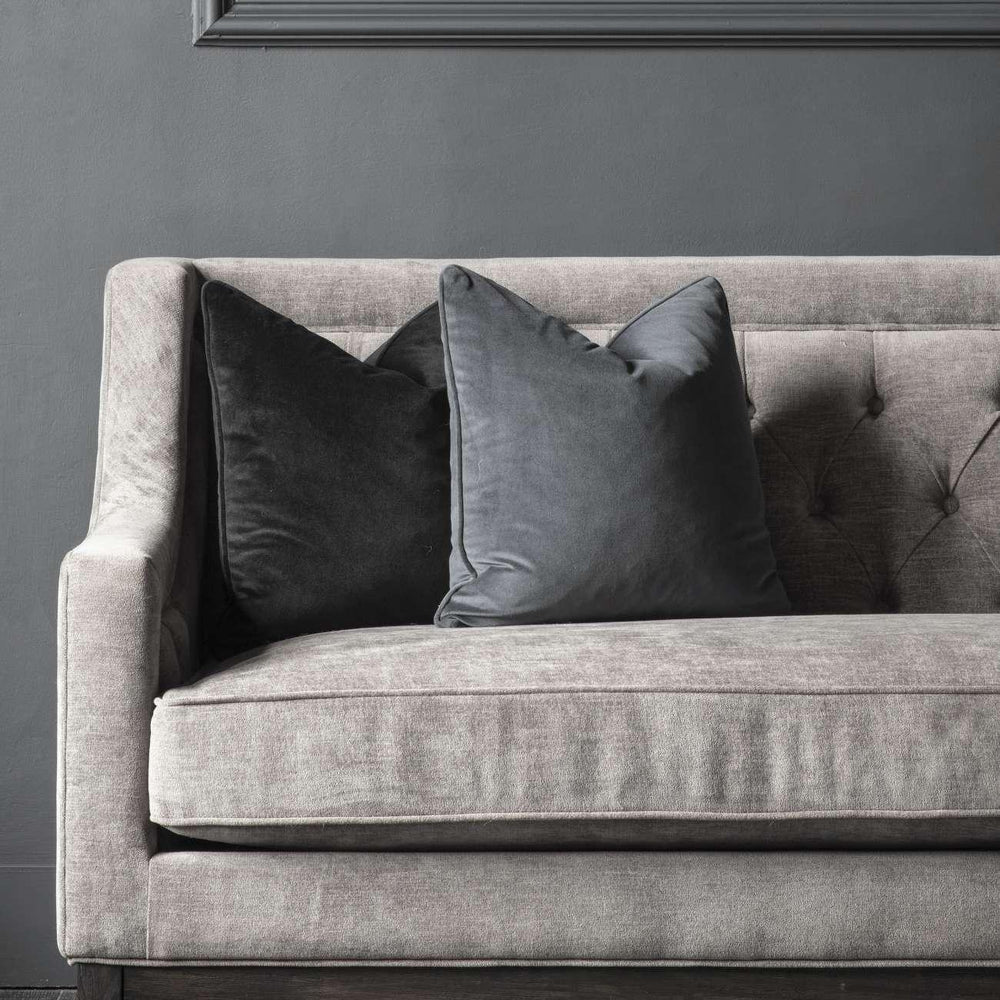 Warm grey fabric sofa with dark cushions against a grey wall.