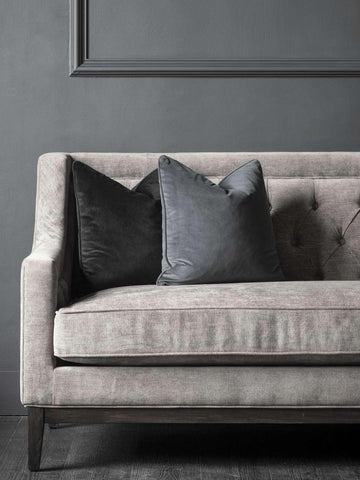 Warm grey fabric sofa with dark cushions against a grey wall.