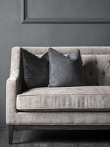 Warm grey fabric sofa with dark cushions against a grey wall.