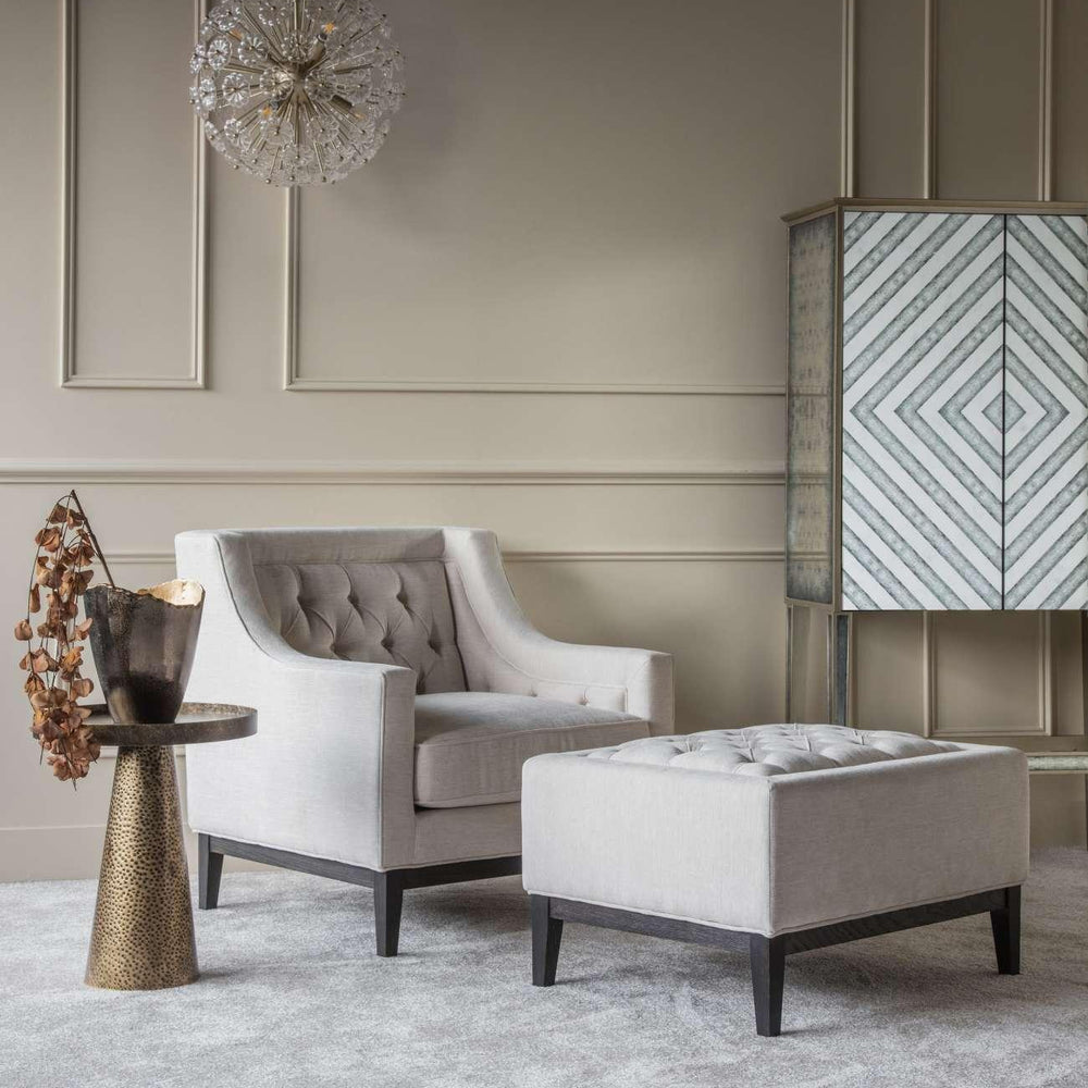 Ivory buttoned stool in elegant living room with armchair and modern decor.