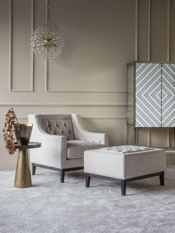 Ivory buttoned stool in elegant living room with armchair and modern decor.