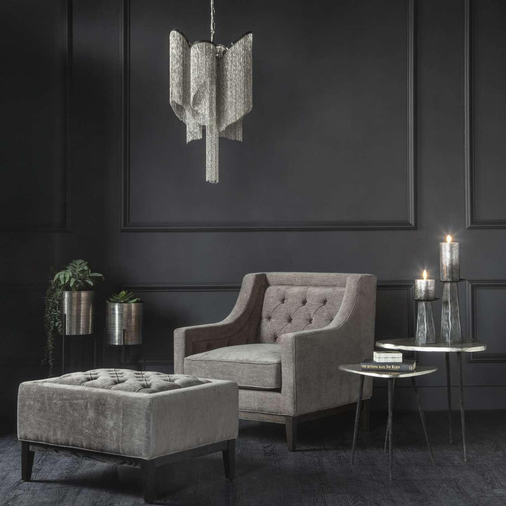 Warm grey buttoned stool in elegant dark living room with armchair and pendant light.