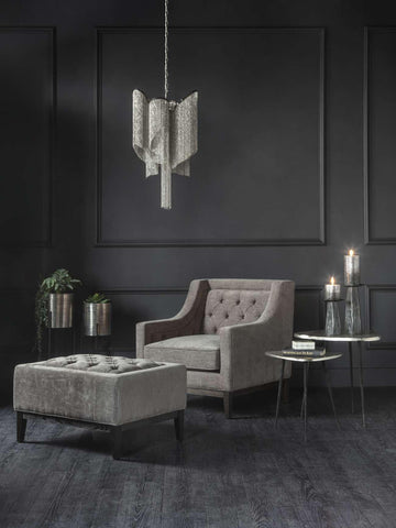 Warm grey buttoned stool in elegant dark living room with armchair and pendant light.