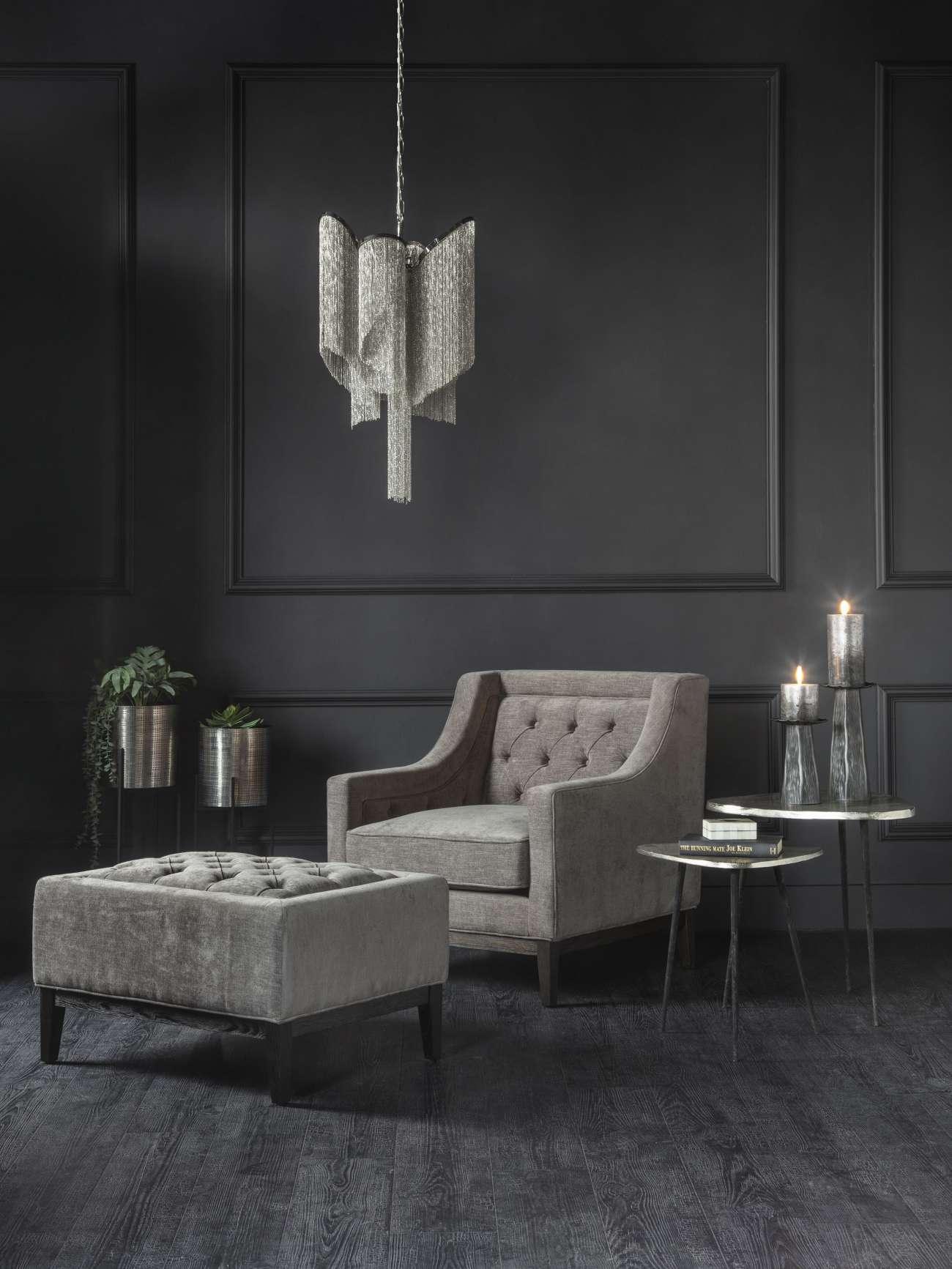 Warm grey buttoned stool in elegant dark living room with armchair and pendant light.