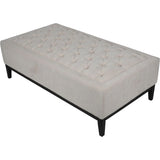 Ivory fabric ottoman with buttoned tufting and dark wooden legs.