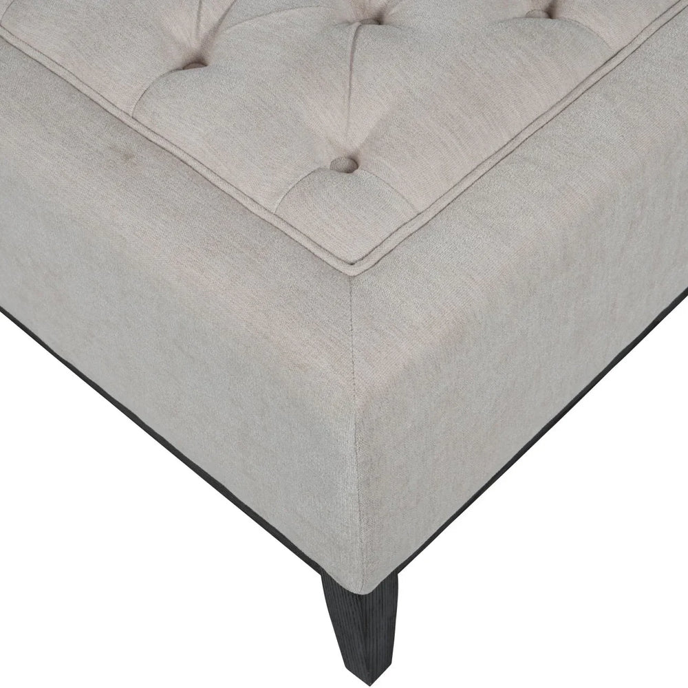 Ivory ottoman corner with button tufting and dark wooden leg.