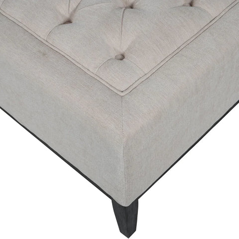 Ivory ottoman corner with button tufting and dark wooden leg.