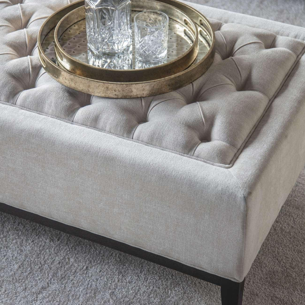 Ivory ottoman with buttoned texture and decorative tray on top.