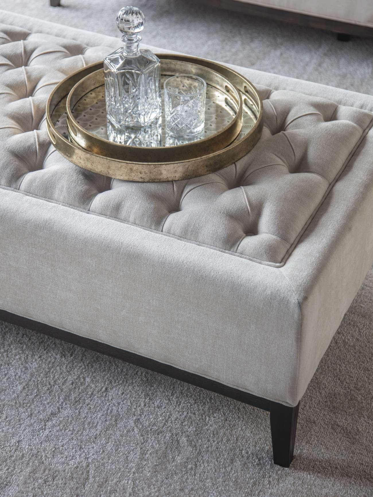 Ivory ottoman with buttoned texture and decorative tray on top.
