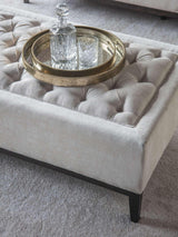 Ivory ottoman with buttoned texture and decorative tray on top.
