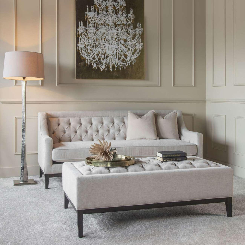 Ivory buttoned ottoman in elegant living room with tufted sofa and chandelier art.