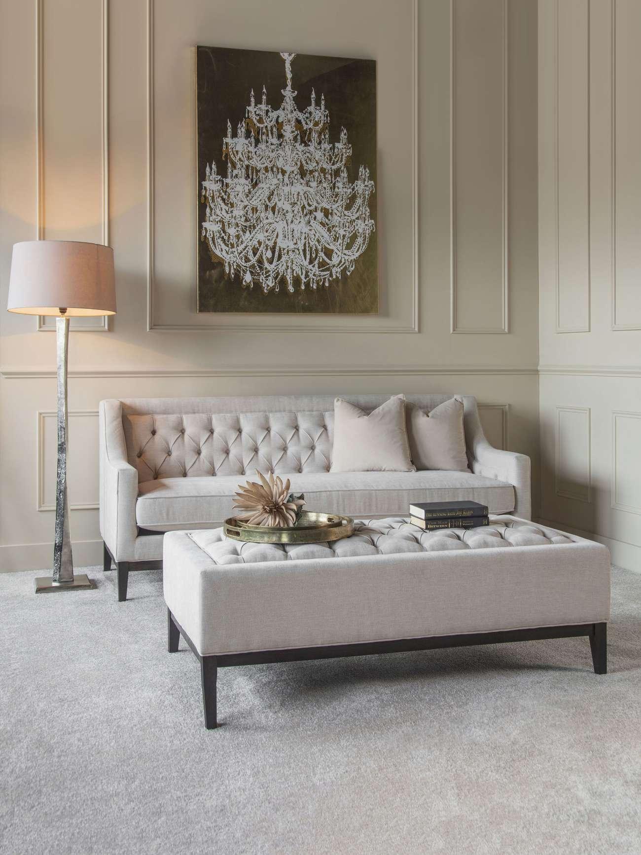 Ivory buttoned ottoman in elegant living room with tufted sofa and chandelier art.