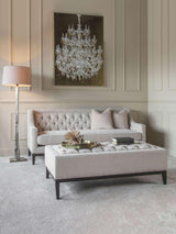 Ivory buttoned ottoman in elegant living room with tufted sofa and chandelier art.