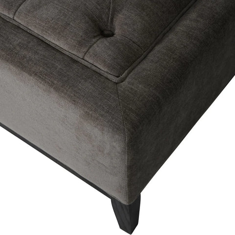 Warm grey fabric ottoman corner with buttoned detail and dark wooden legs.