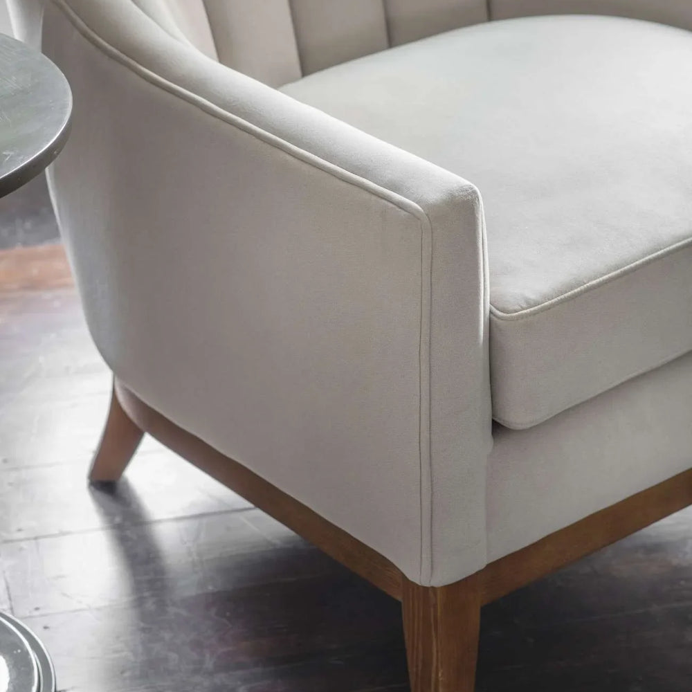 Taupe upholstered chair with wooden legs on dark wood floor.