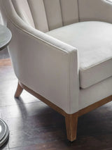 Taupe upholstered chair with wooden legs on dark wood floor.