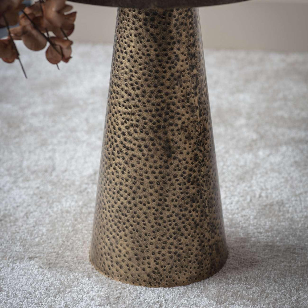 Textured antique gold side table base on light carpet.