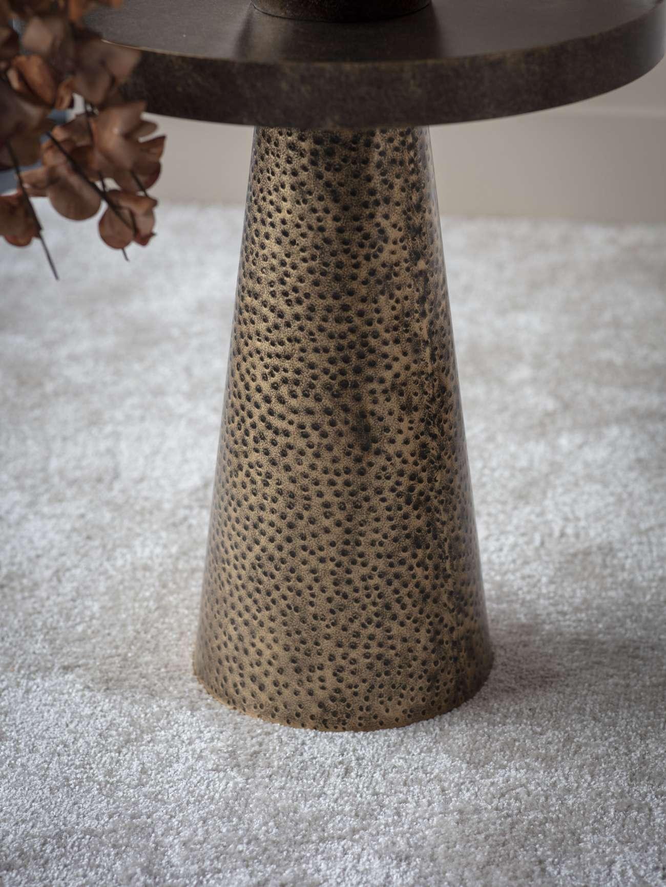 Textured antique gold side table base on light carpet.