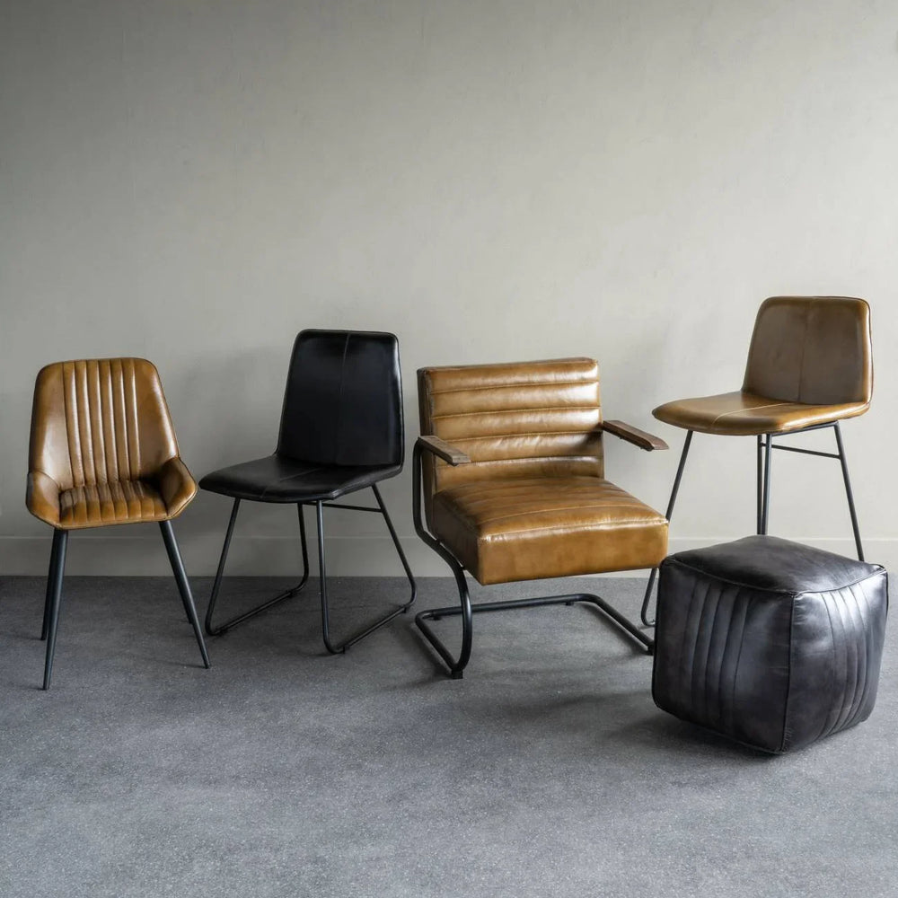 Charcoal and tan leather dining chairs with a matching pouf on a grey floor.
