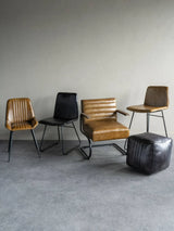 Charcoal and tan leather dining chairs with a matching pouf on a grey floor.
