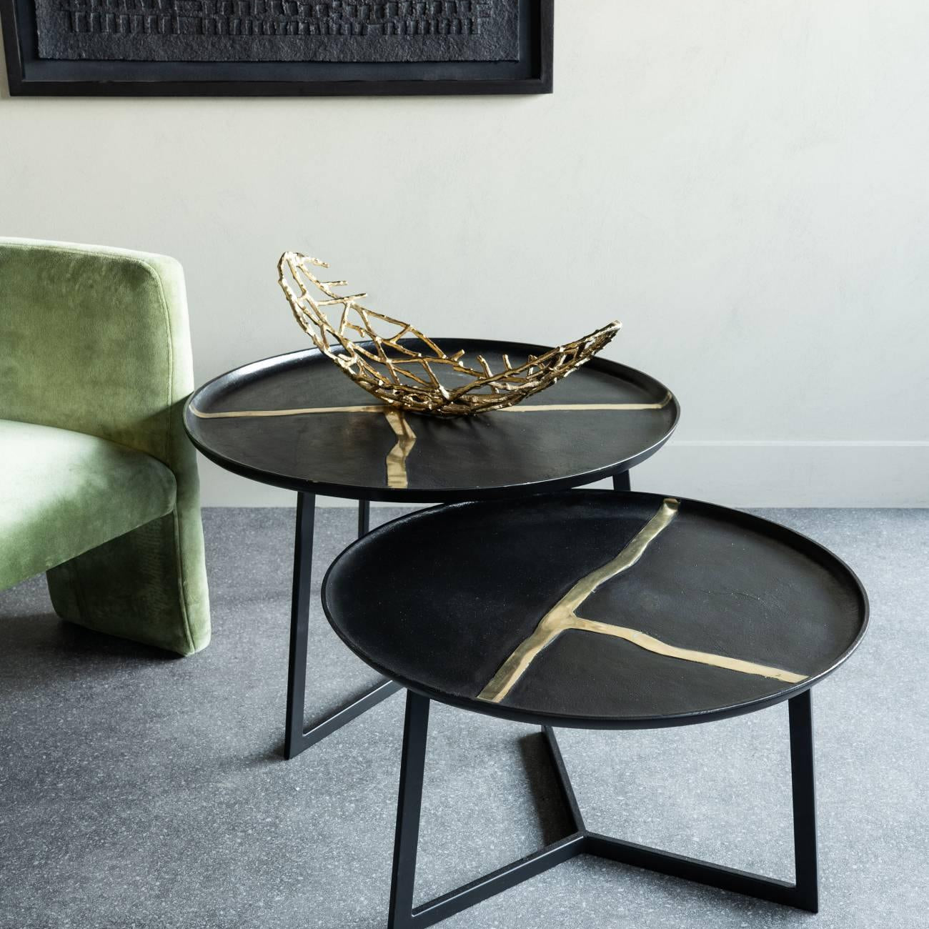 Black round tables with gold accents beside a green chair in a modern room.