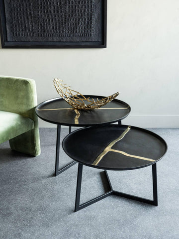 Black round tables with gold accents beside a green chair in a modern room.