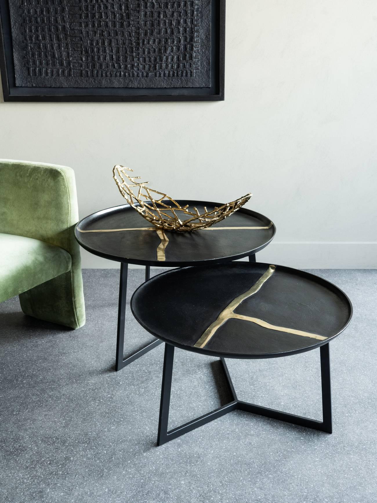 Black round tables with gold accents beside a green chair in a modern room.