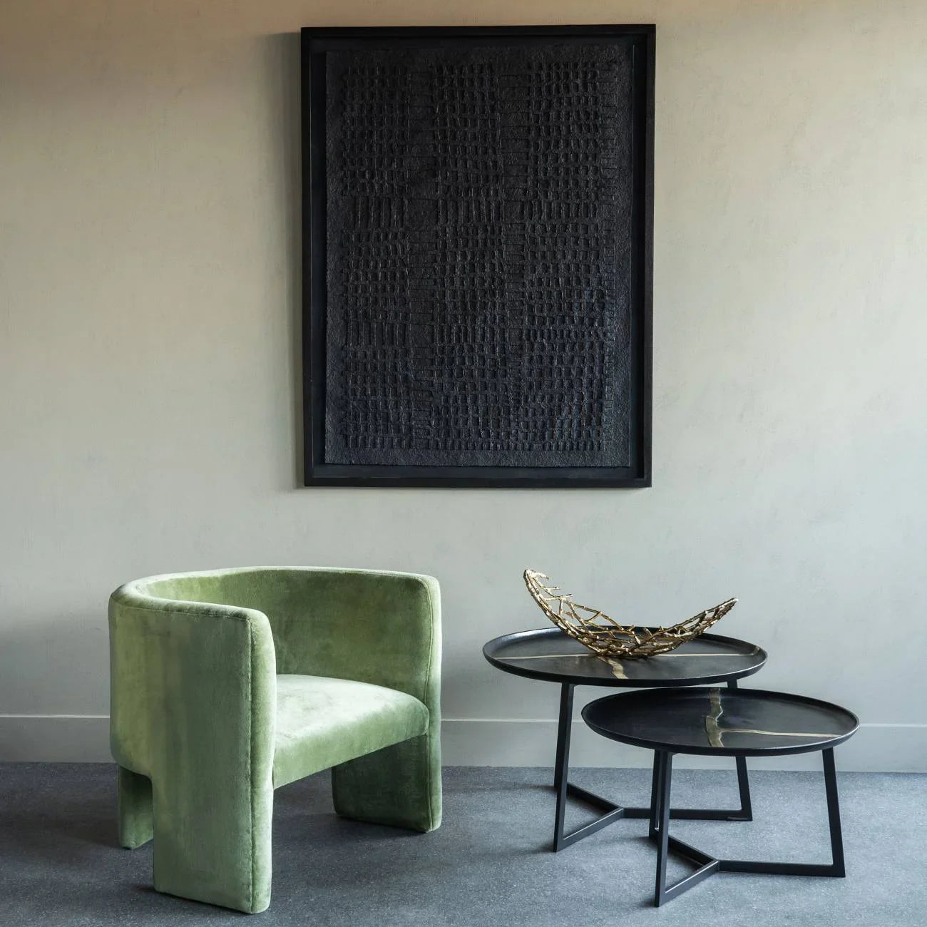 Black metal coffee tables in modern room with green velvet chair and abstract wall art.