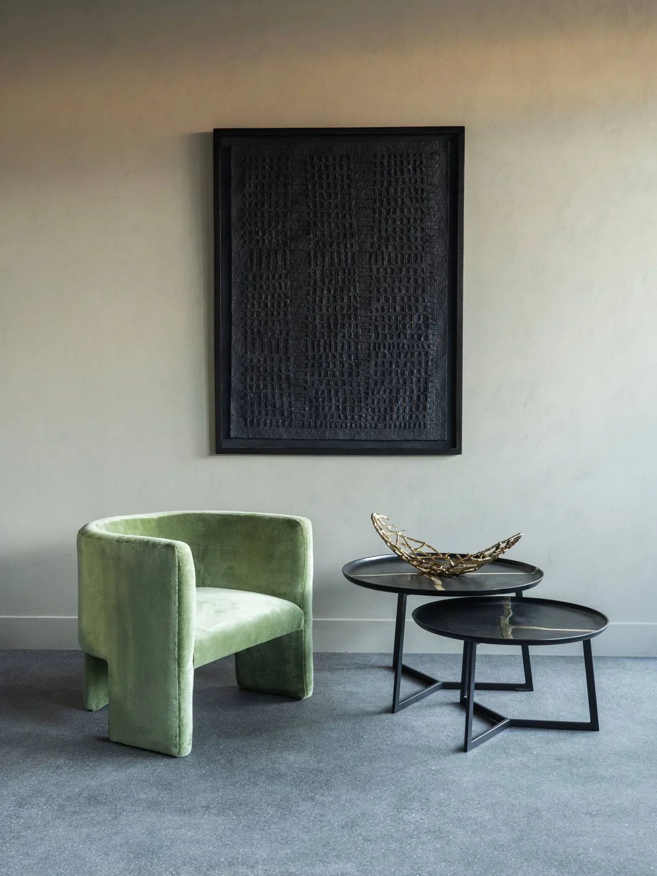Black metal coffee tables in modern room with green velvet chair and abstract wall art.