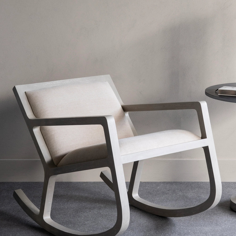 Beige cushioned rocking chair on grey floor in a minimalist room.
