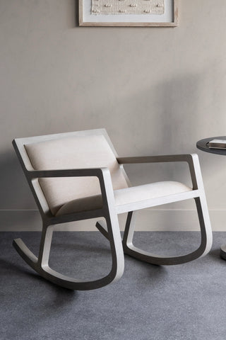 Beige cushioned rocking chair on grey floor in a minimalist room.