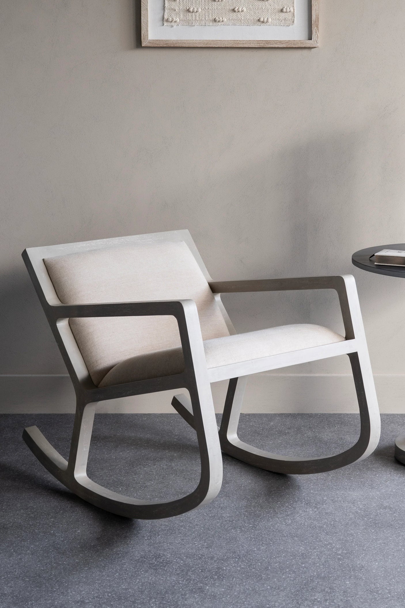 Beige cushioned rocking chair on grey floor in a minimalist room.