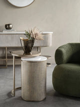 Aged gold nesting tables with a vase beside a green armchair in a stylish room.