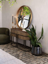 Gold console table with round mirror, styled with plants and candles on cobblestone floor.