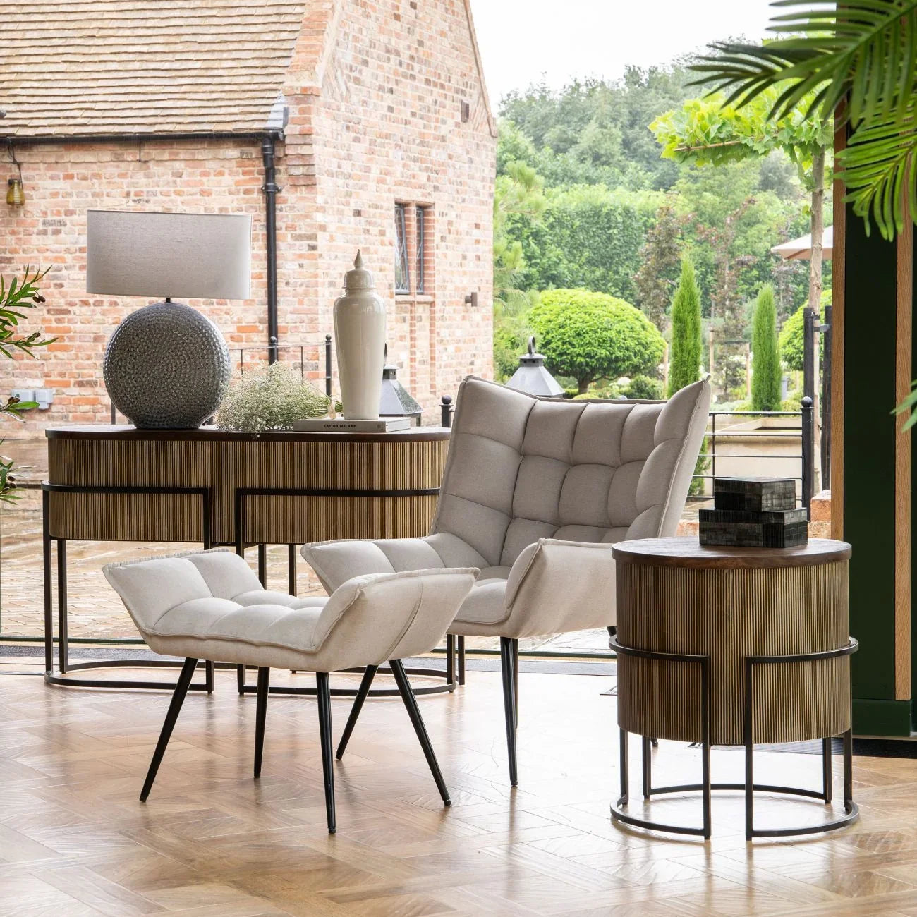 Beige armchair and ottoman in a bright room with gold console and round side table.