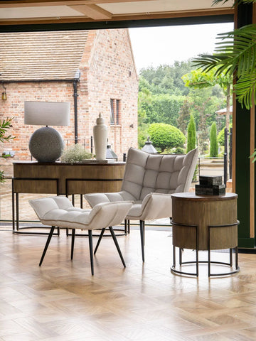 Beige armchair and ottoman in a bright room with gold console and round side table.