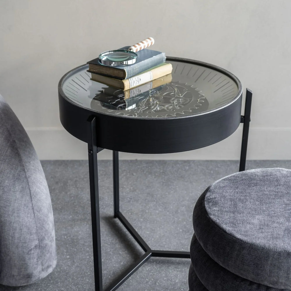 Black metal side table with glass top displaying books and a magnifying glass.